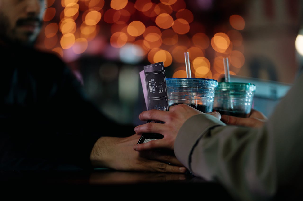 Home Close-up of hands exchanging cinema tickets and plastic cup drinks with straws.